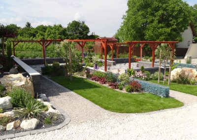 Flamingó Panzió parkja - Járdák mentén elterülő gyep és évelőágyások, felettük lugasok magasodnak.