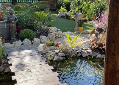 Cikcakkos szélű fahíd, vele szemben egy álló Buddha